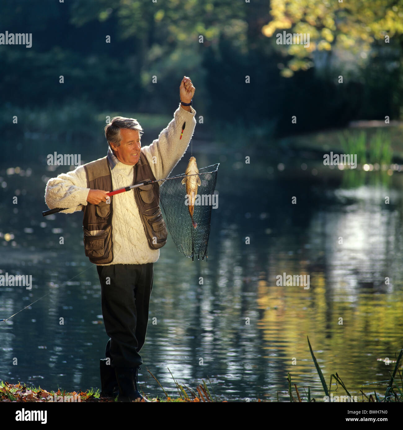 Senior Angler an einem Teich mit einem Fisch im Netz Stockfoto