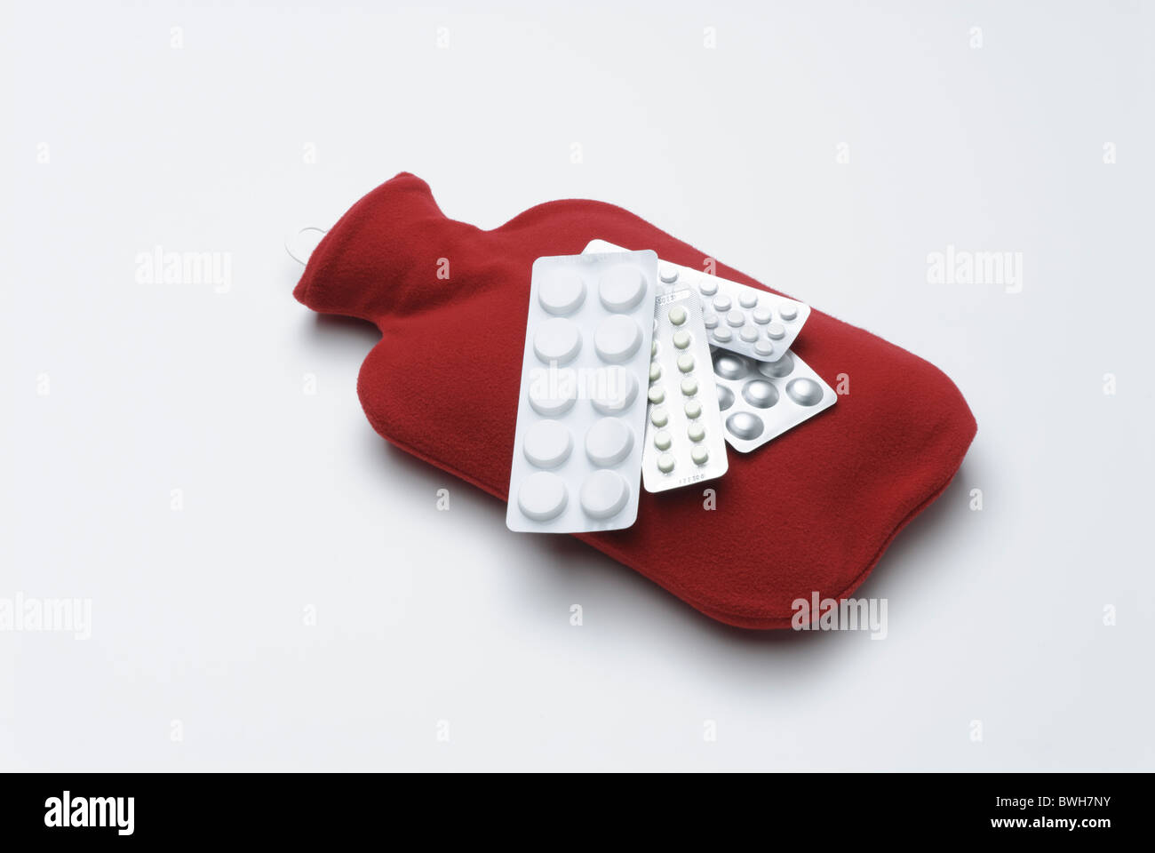 Wärmflasche mit rotem Einband und Tabletten in Blisterpackungen Stockfoto