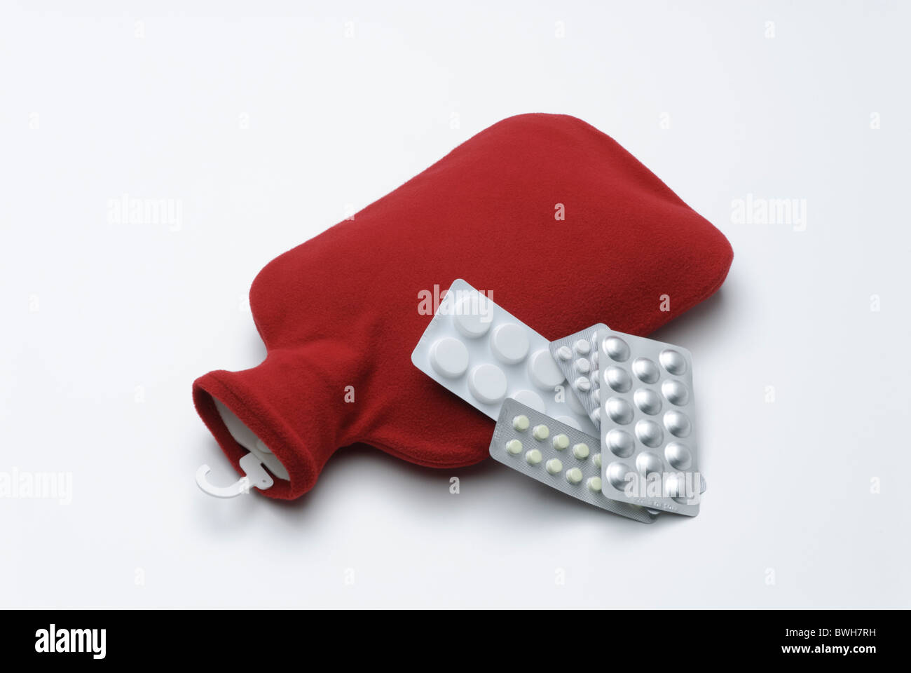 Wärmflasche mit rotem Einband und Tabletten in Blisterpackungen Stockfoto