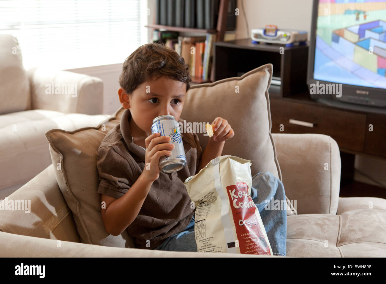 Vier-jährige mexikanisch-amerikanischen jungen frisst Kartoffelchips und nippt Softdrink im Wohnzimmer in seinem Haus in Austin, Texas Stockfoto