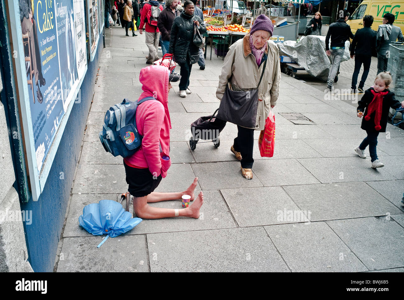 Ein Mann mit einer schweren Bein Fehlstellung bittet an der Moore Street, wie eine alte Frau und Kind vorbeigehen. Stockfoto