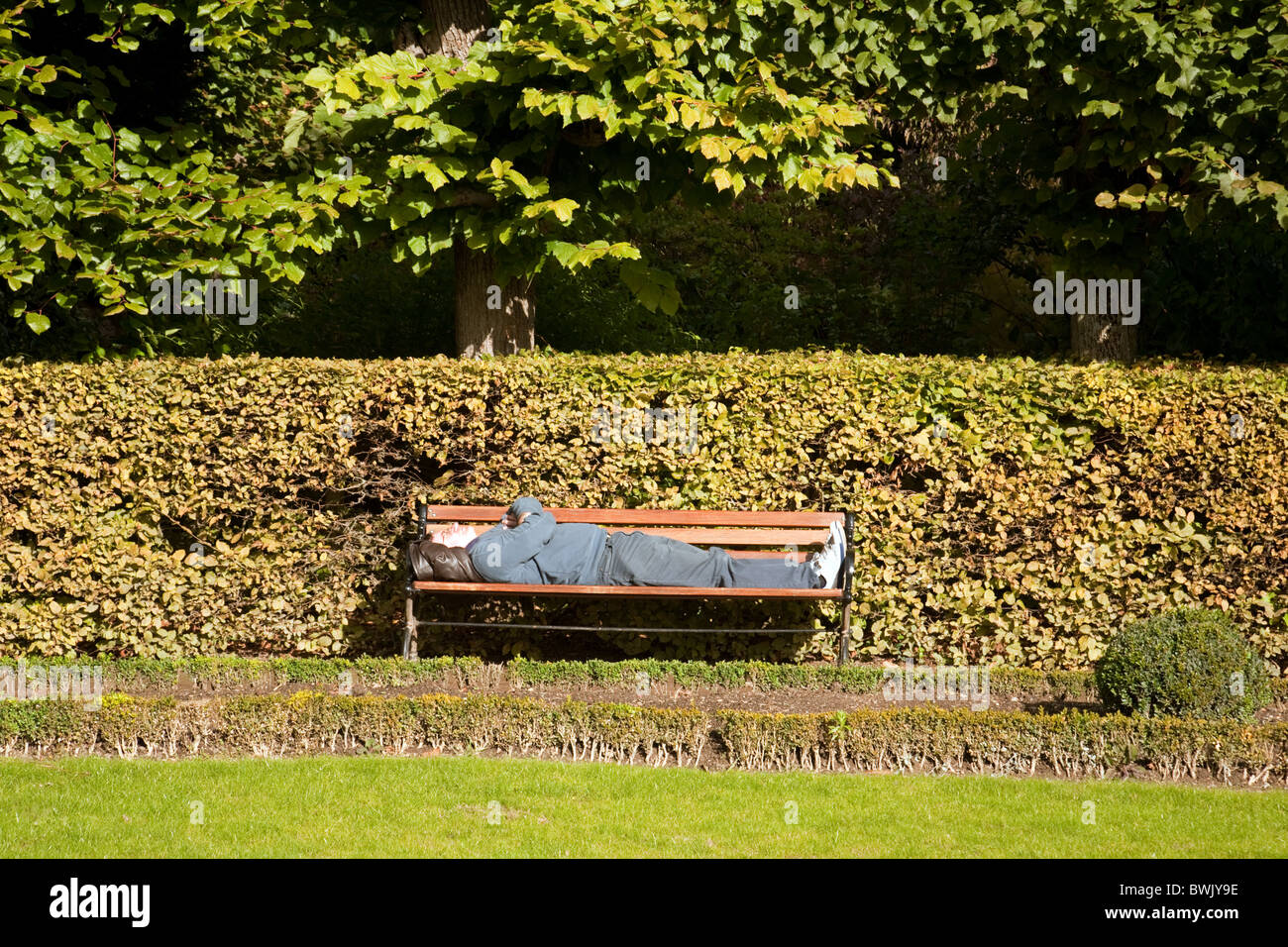 Ein Mann schlief auf einer Parkbank in der Nachmittagssonne Stockfoto