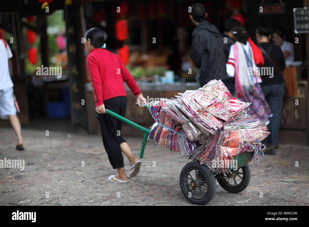 Eine einheimische Frau, die Transport von Gütern in der Altstadt von Lijiang, Yunnan Provinz, China. Stockfoto