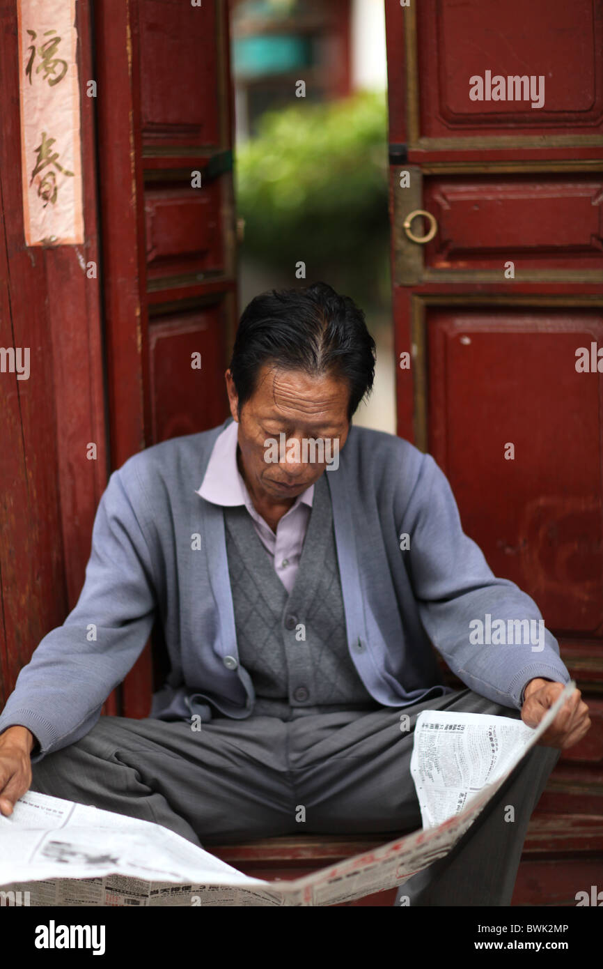 Ein Mann liest eine chinesische Zeitung in der Altstadt von Lijiang, Yunnan Provinz, China. Stockfoto