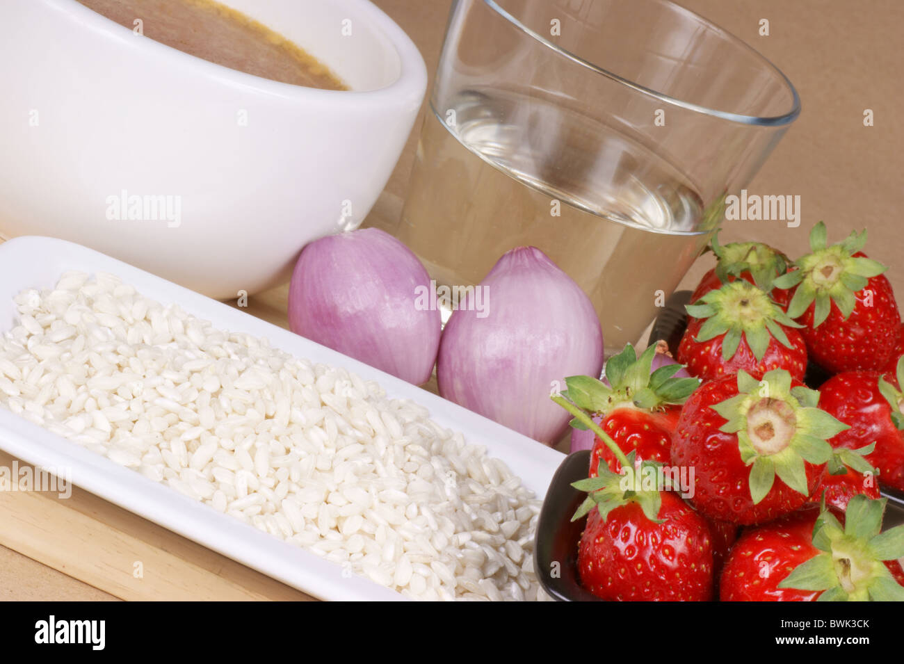 Zutaten für Risotto mit Erdbeeren: weißer Reis, Erdbeeren, Zwiebeln, Weißwein und Gemüsebrühe ablöschen. Stockfoto