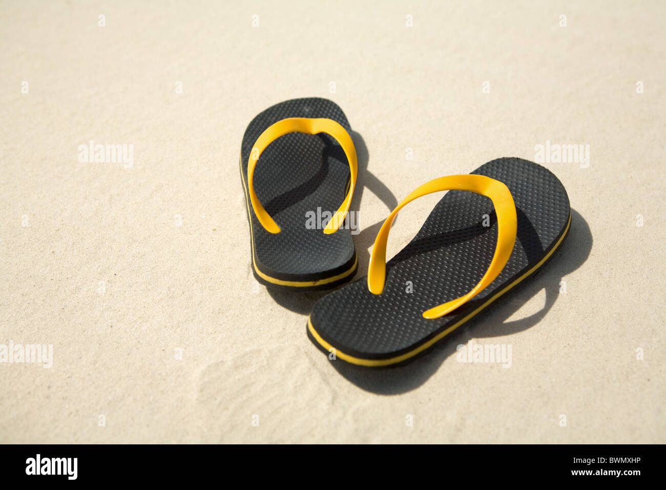 Bild von paar gelbe und schwarze Flipflops am Sandstrand Stockfoto