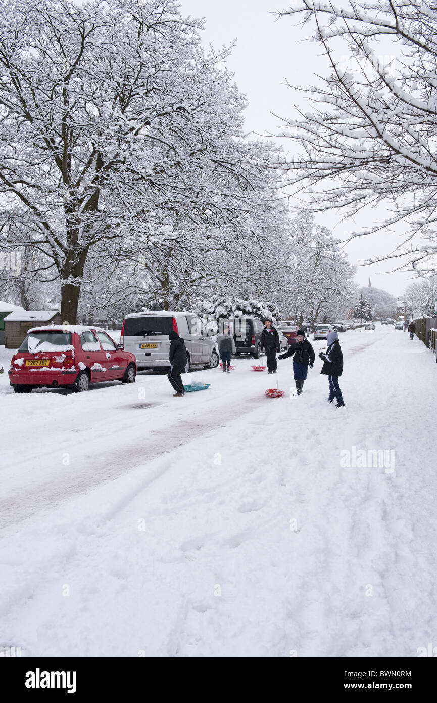 Kinder ziehen ihre Schlitten auf einer verschneiten Straße. Stockfoto