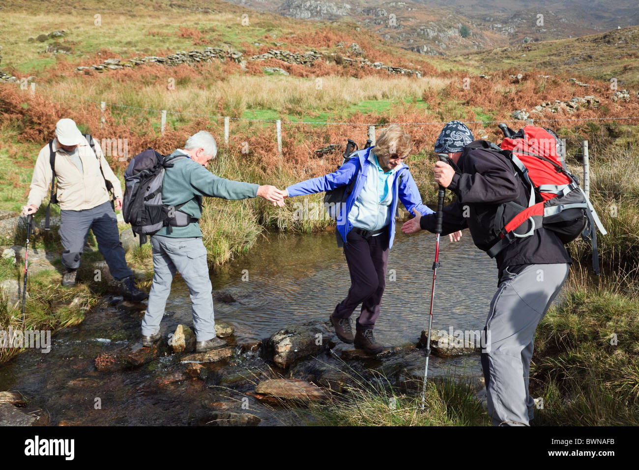 Zwei Männer einer Frau Walker, überqueren einen Bach bei einem Spaziergang im Snowdonia National Park, North Wales, UK eine helfende Hand geben. Stockfoto