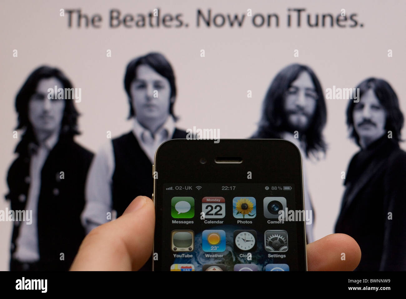 Ein Apple iPhone 4 mit der Apple-Website im Hintergrund zeigt die Beatles, jetzt erhältlich auf iTunes Stockfoto