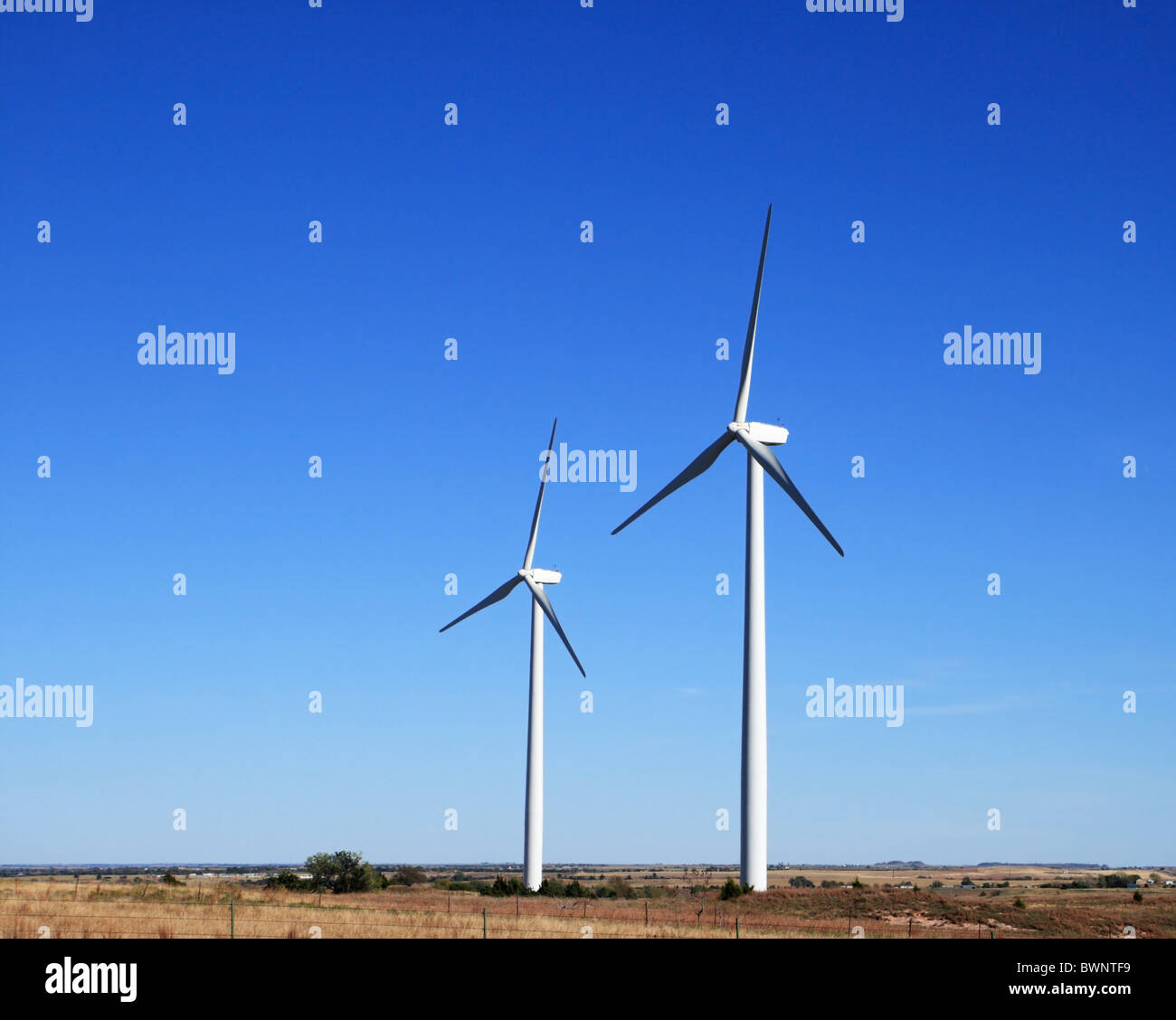 zwei weiße elektrische Windmühlen oder Windkraftanlagen auf einer flachen Prärie mit blauem Himmel Hintergrund und Kopie Stockfoto