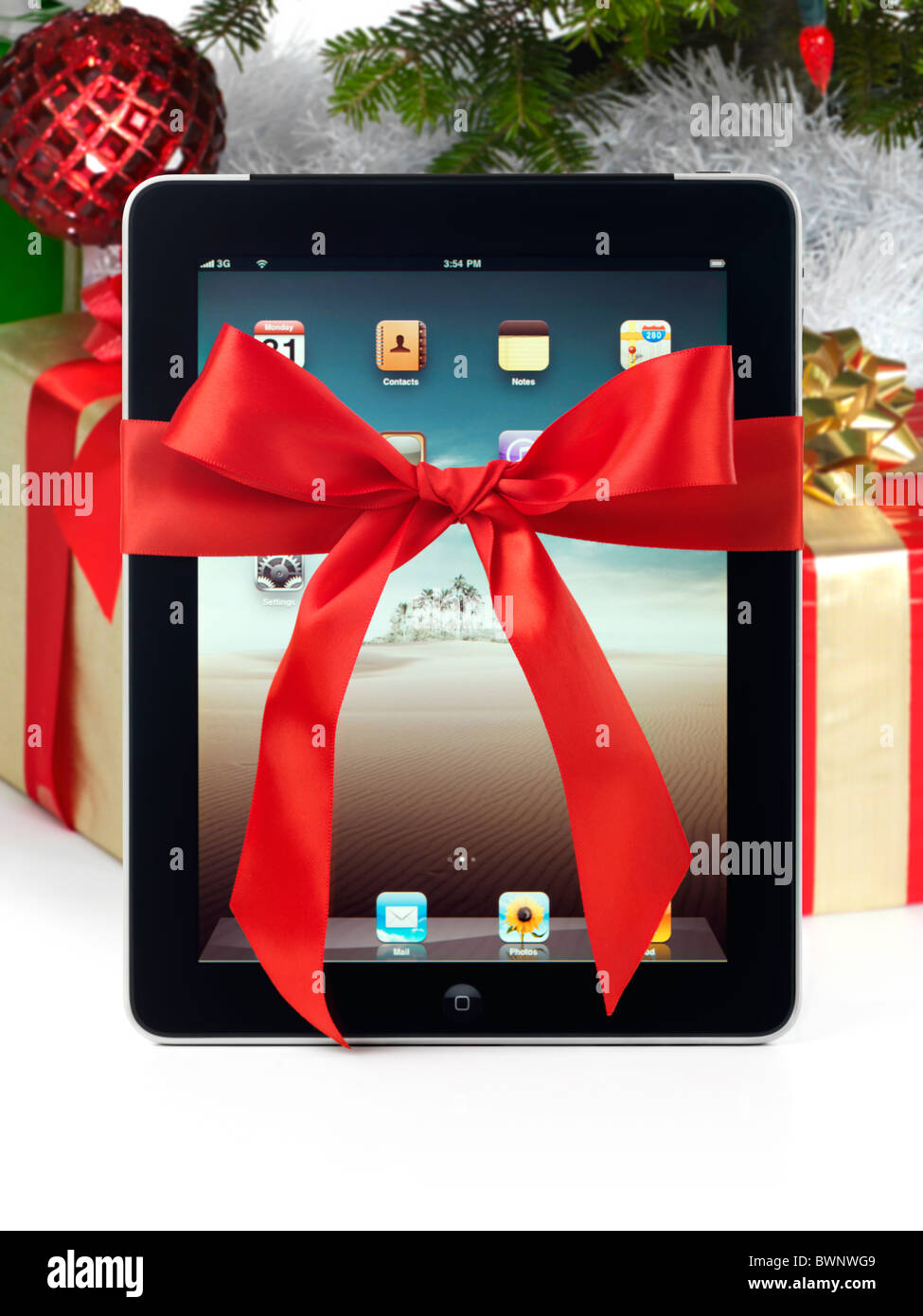 Apple iPad 3G Tablet mit einer roten Geschenk-Schleife gebunden drumherum stehen unter einem Weihnachtsbaum mit Geschenken Stockfoto