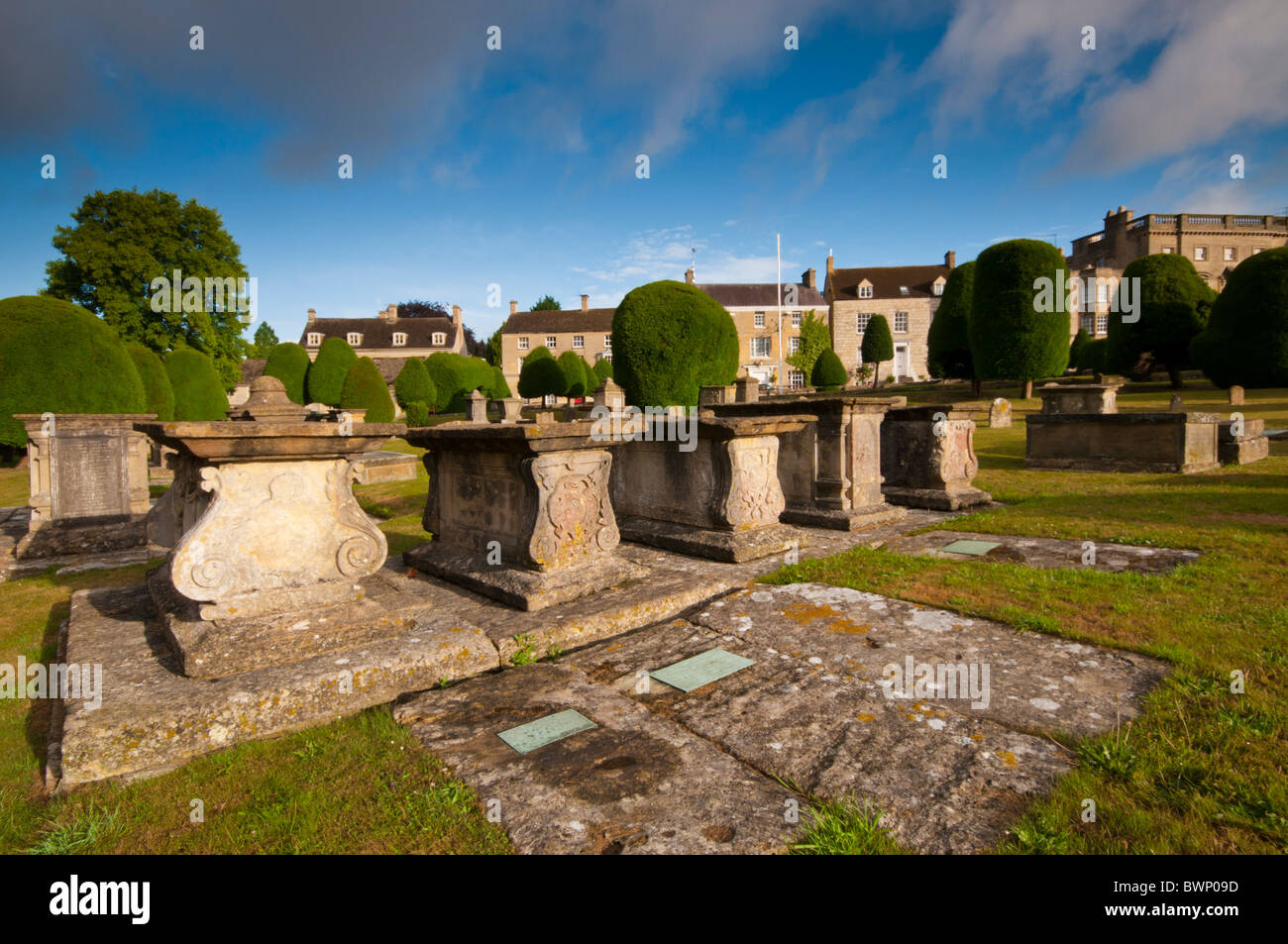 Str. Marys Kirchhof mit Eiben und Cotswold Steinhütten im Hintergrund, Painswick, Gloucestershire, UK Stockfoto