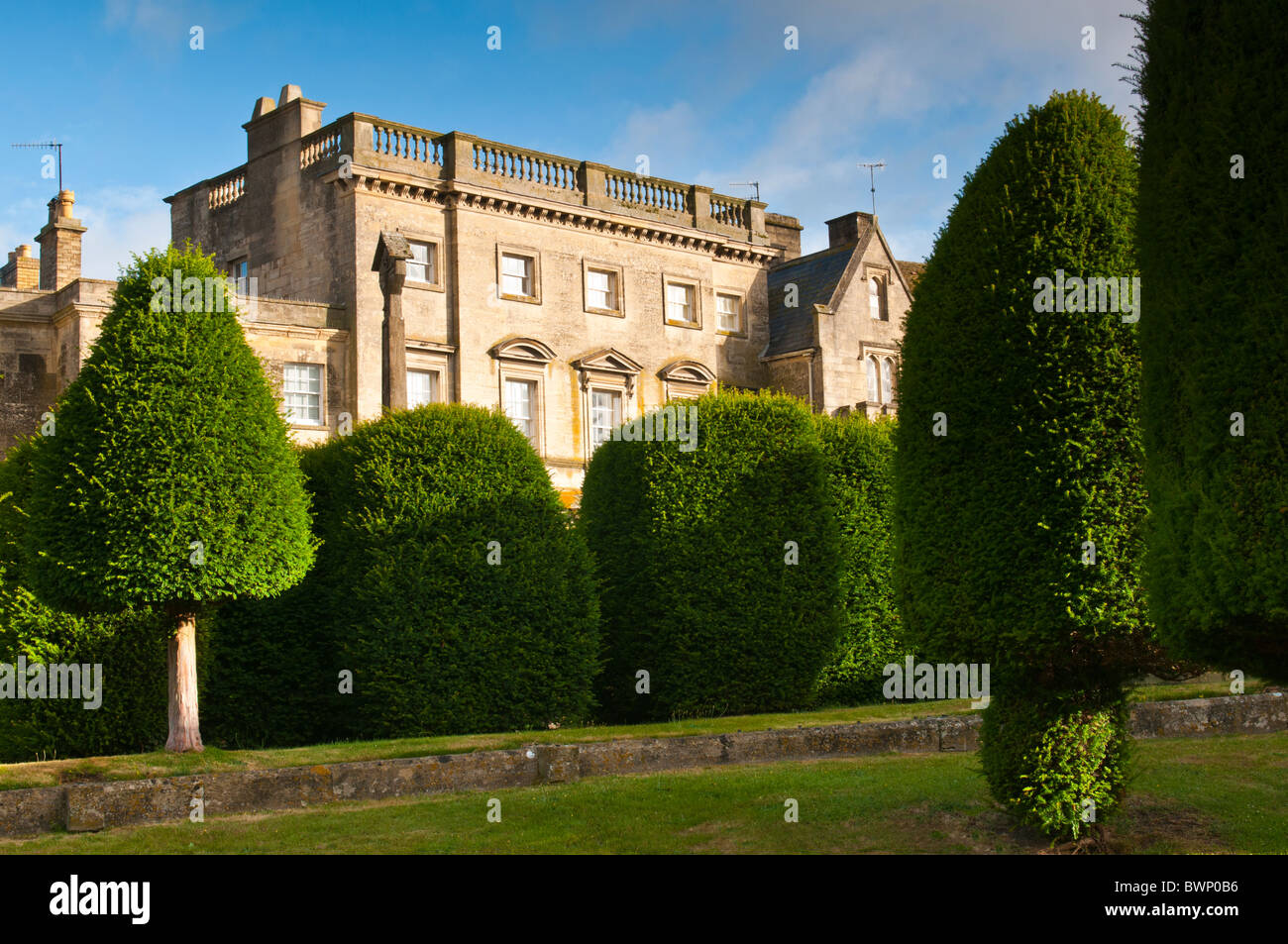 Str. Marys Kirchhof mit Eiben und Cotswold Steingebäude im Hintergrund, Painswick, Gloucestershire, UK Stockfoto