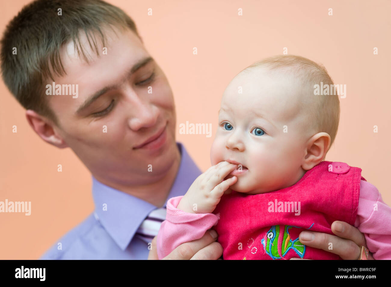 Europäische junger Mann schaut liebevoll seine kleine Tochter, die ihre Finger in den Mund nahm Stockfoto