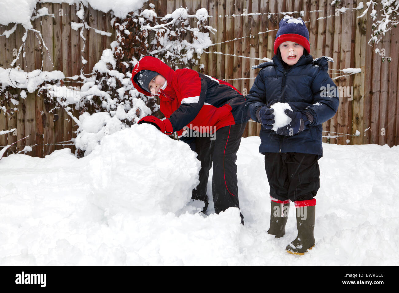 Zwei Jungen, die im Schnee spielen, eine mit einem schneeball und ein weiterer, der einen Schneemann zu bauen. Stockfoto