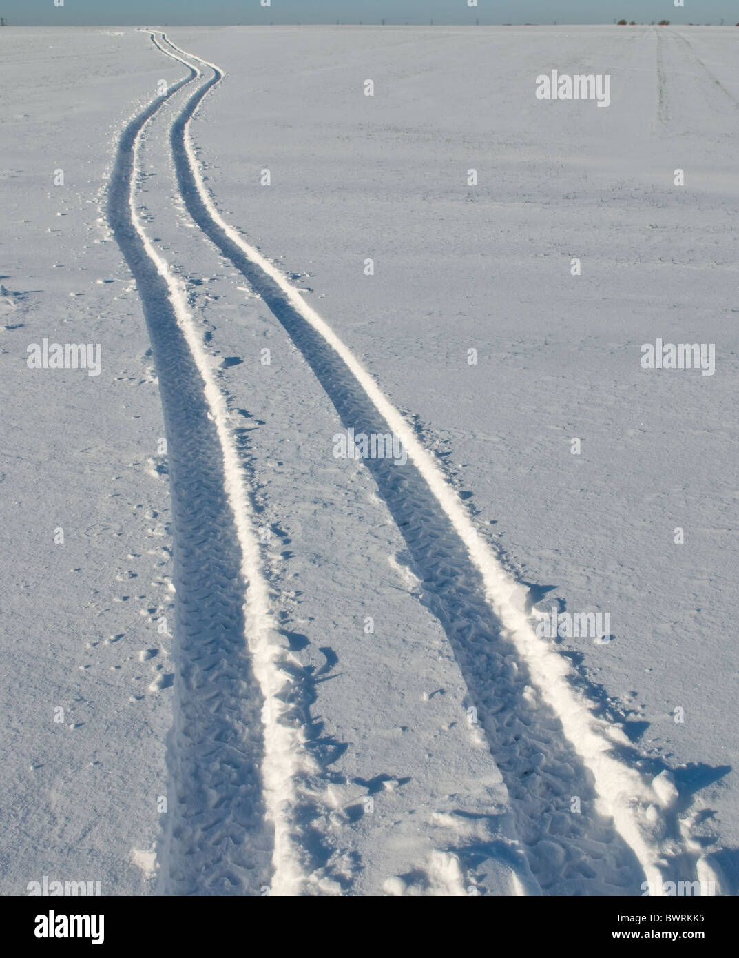 Fahrbare Strecken gemacht von einem Bauernhof-Fahrzeug auf einem schneebedeckten Feld. Stockfoto