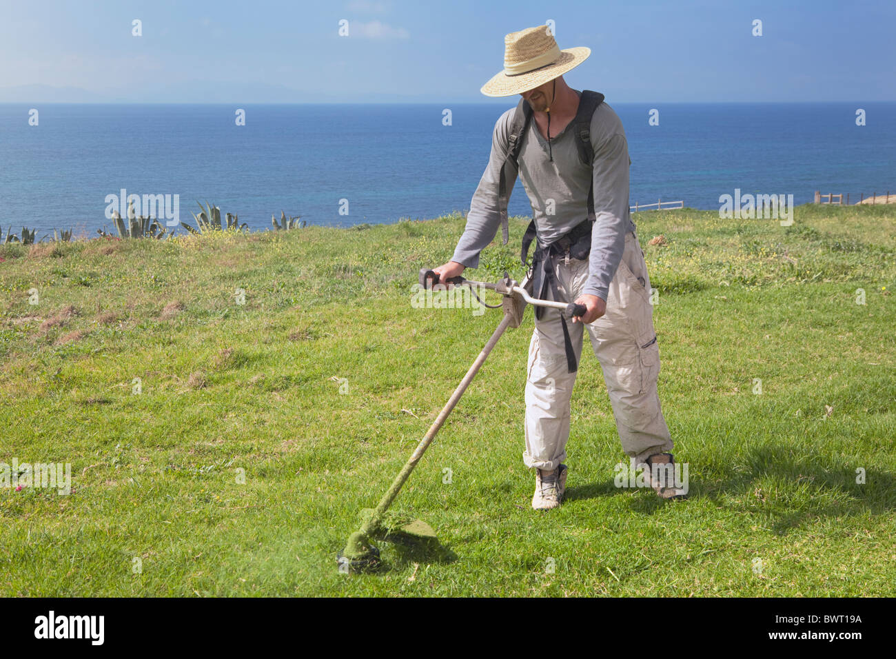 Mann Strimming Rasen mit Ozean hinter Stockfoto