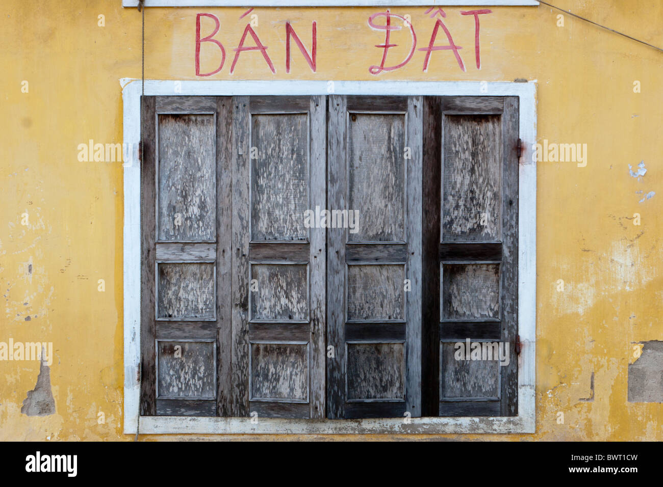 Alten hölzernen Doppeltüren inmitten ein weißer Rahmen gegen eine gelbe Wand mit den vietnamesischen Wörtern "Ban Dat" in rot lackiert Stockfoto