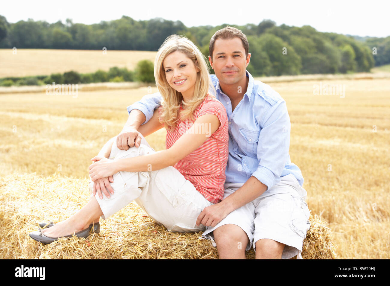 Paar sitzt auf Strohballen In abgeernteten Feld Stockfoto