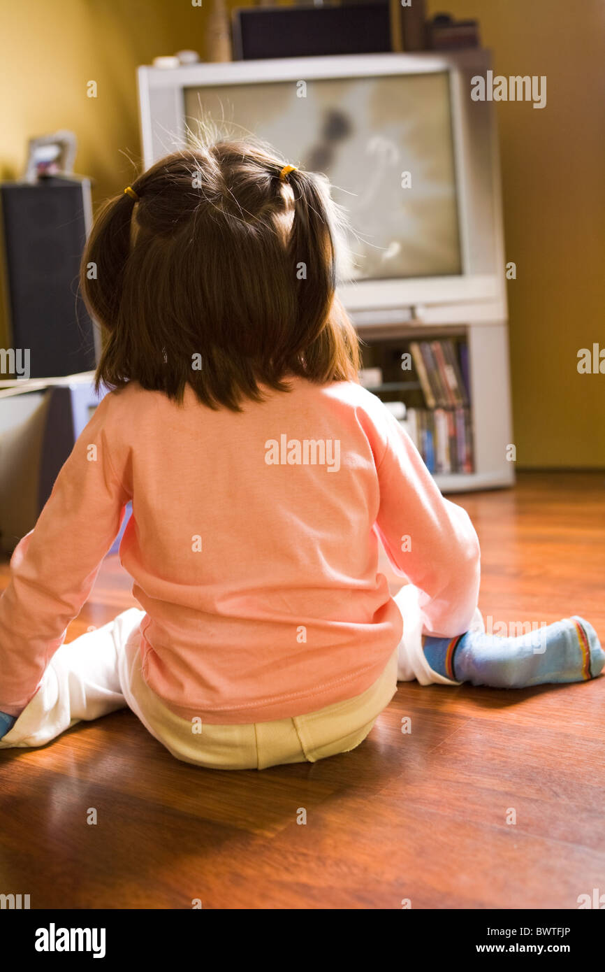Heckansicht des kleines Mädchen auf dem Boden sitzend und Zeichentrickfilme im Fernsehen zu Hause Stockfoto