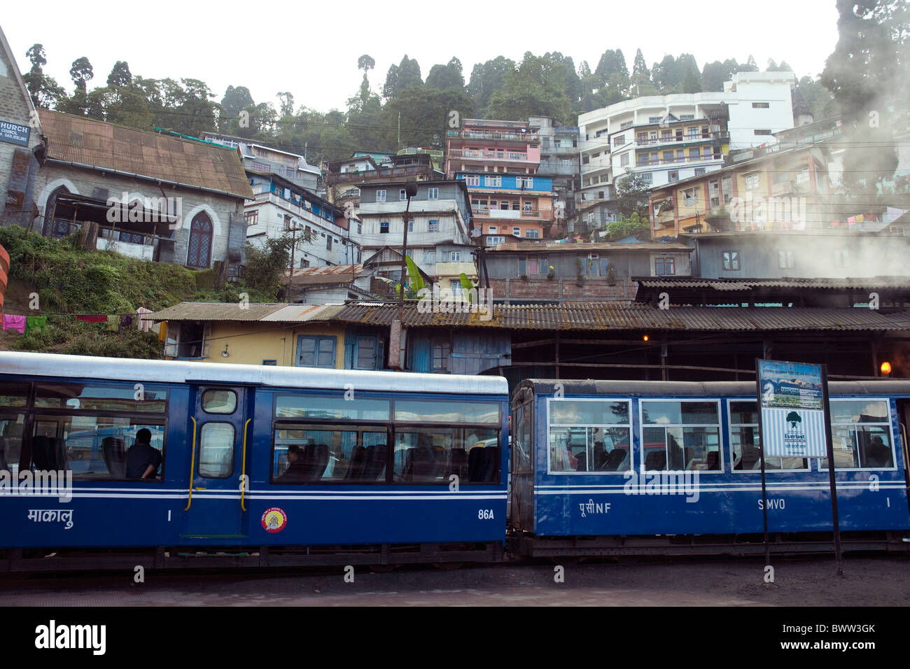 Ein Zug der Darjeeling-basierte Himalaya Bahn verkehrt auf der engen Strecke unterhalb Hügel Stadthäuser Stockfoto
