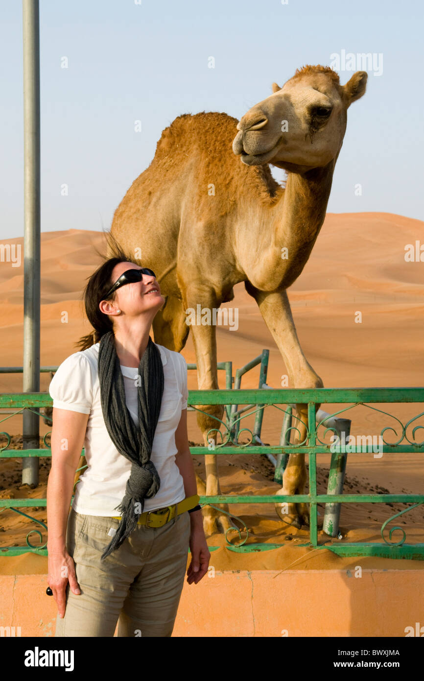 Glückliche Frau blickte zu einem Kamel mit Wüste Sanddünen im Hintergrund Stockfoto