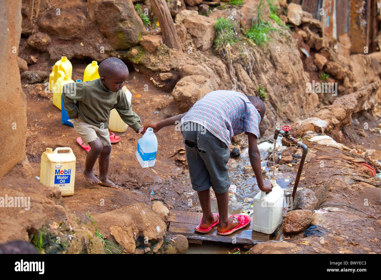 Jungen Behälter einfüllen von Wasser aus einem Hahn in den Kibera Slums, Nairobi, Kenia Stockfoto