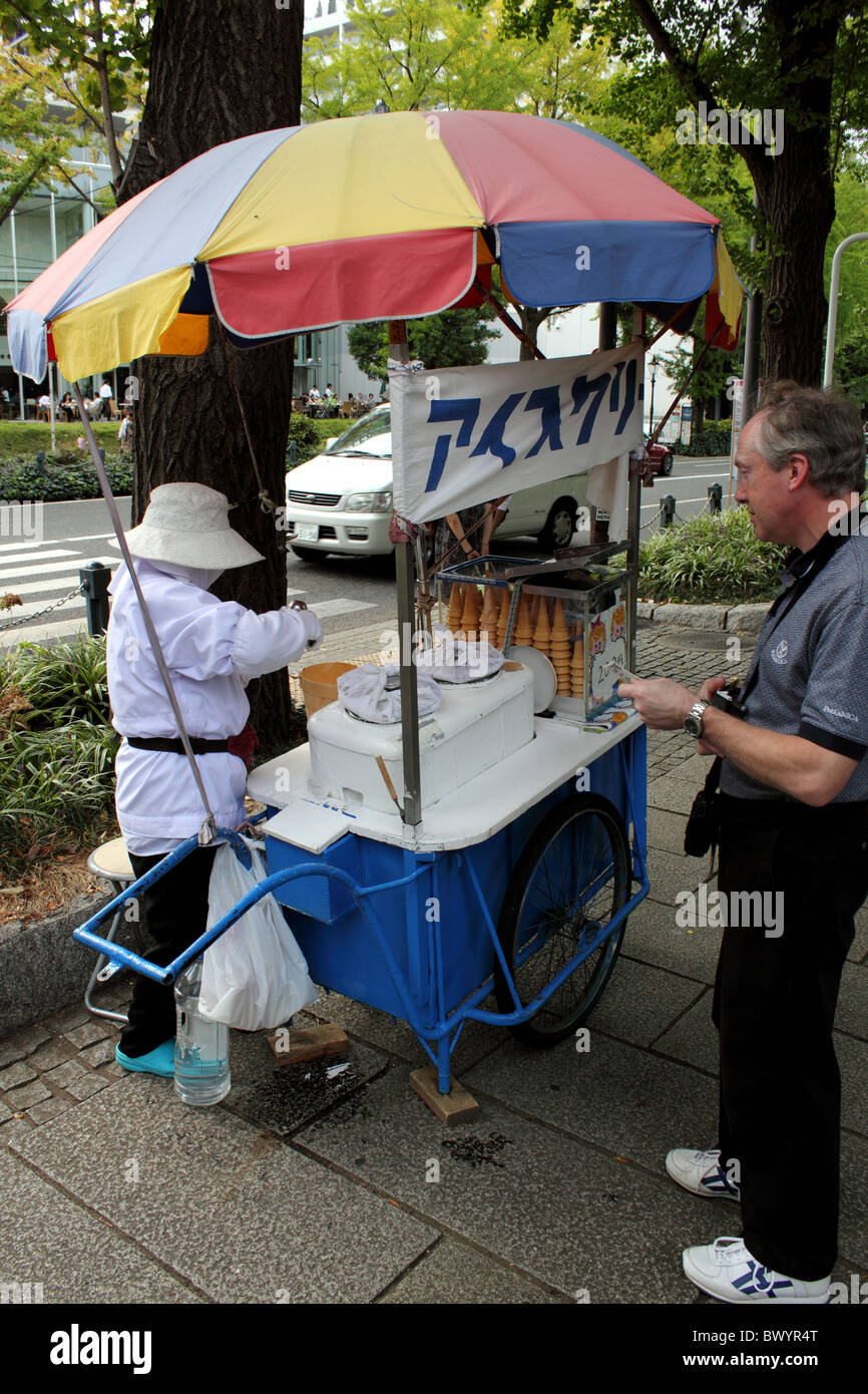 Westliche Mensch kauft Eis von einer älteren Frau, gekleidet in weiß auf einer Straße Warenkorb in Yokohama Japan Stockfoto