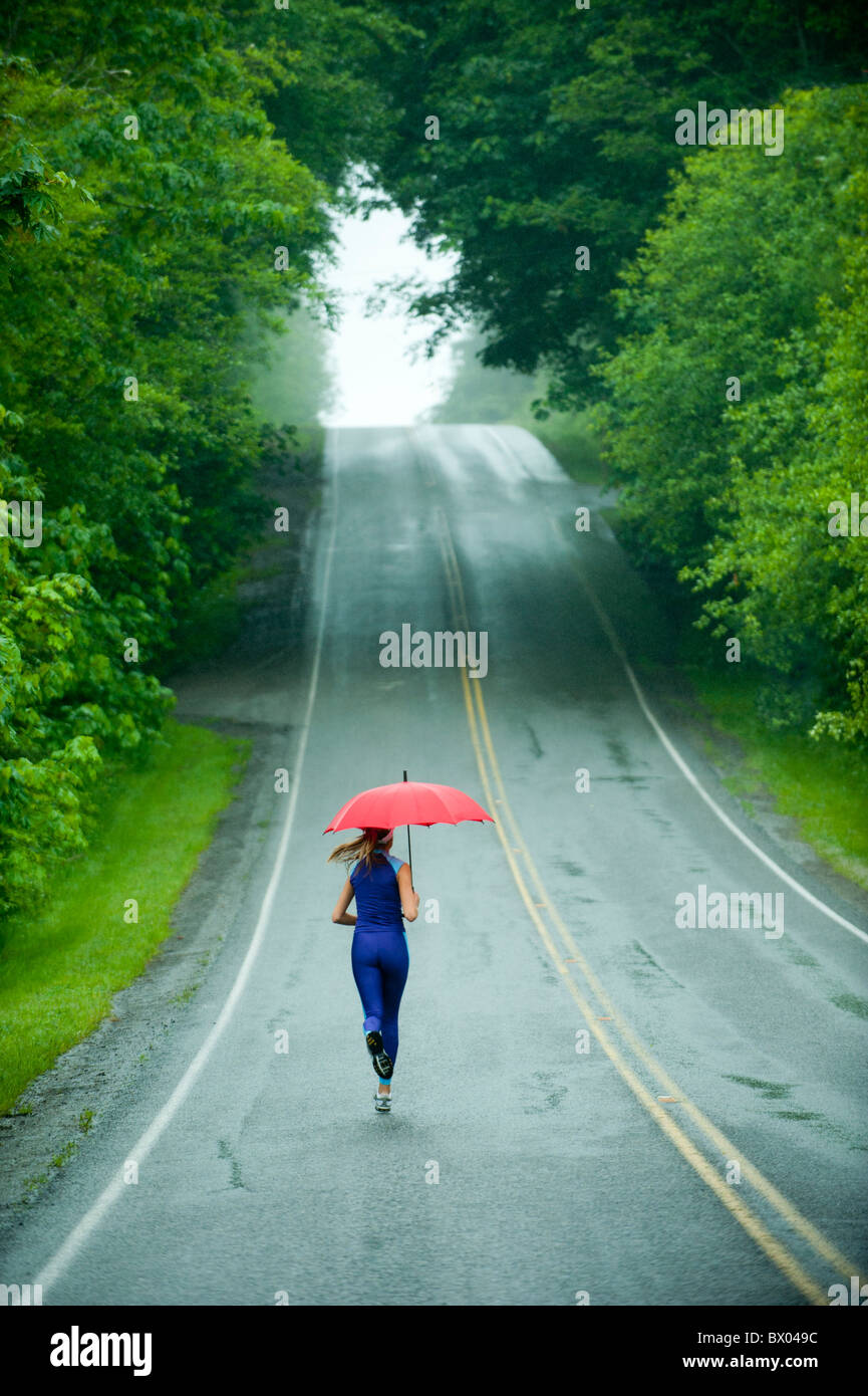 Kaukasische Frau, die auf remote-Straße mit Regenschirm Stockfoto