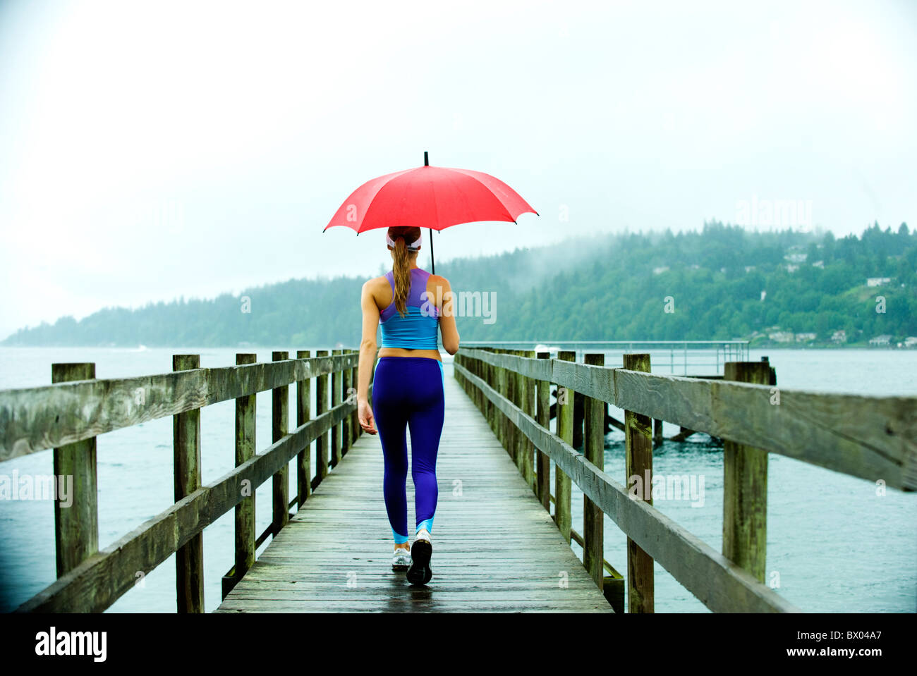 Kaukasischen Frau in Sportkleidung mit roten Regenschirm am pier Stockfoto