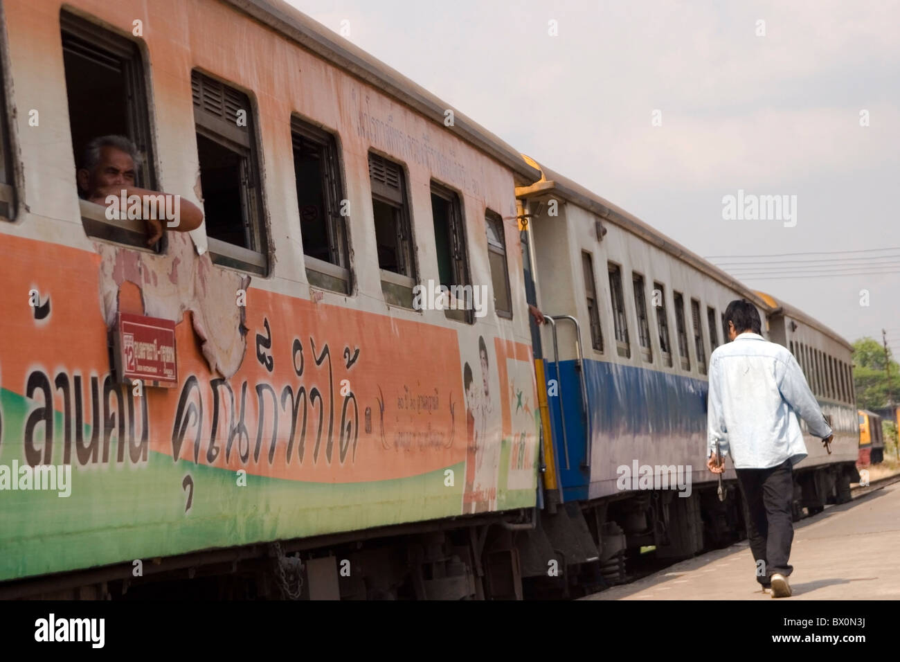 Ein männlicher Eisenbahner spaziert vorbei an Pkw Eisenbahn Zug am Bahnhof in Ubon Ratchathani, Thailand. Stockfoto