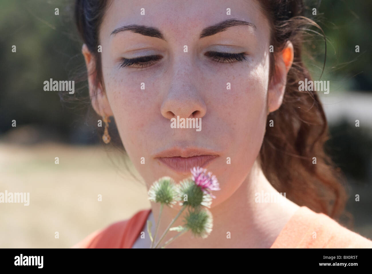 Ehrliches Porträt eines Brünette junge Frau mit einem Thistle Blume. Stockfoto