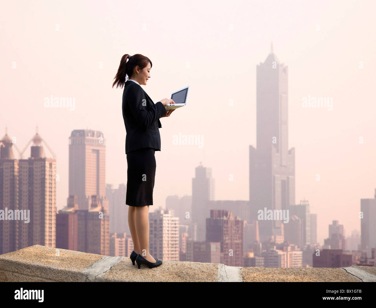 Geschäftsfrau mit Computer und Stand auf der Spitze eines Wolkenkratzers mit Stadtbild Stockfoto