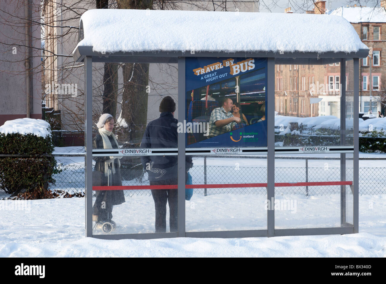 Ein Mann und eine Frau warten auf einen Bus im Schnee in einer Wartehalle, Edinburgh, Schottland Stockfoto