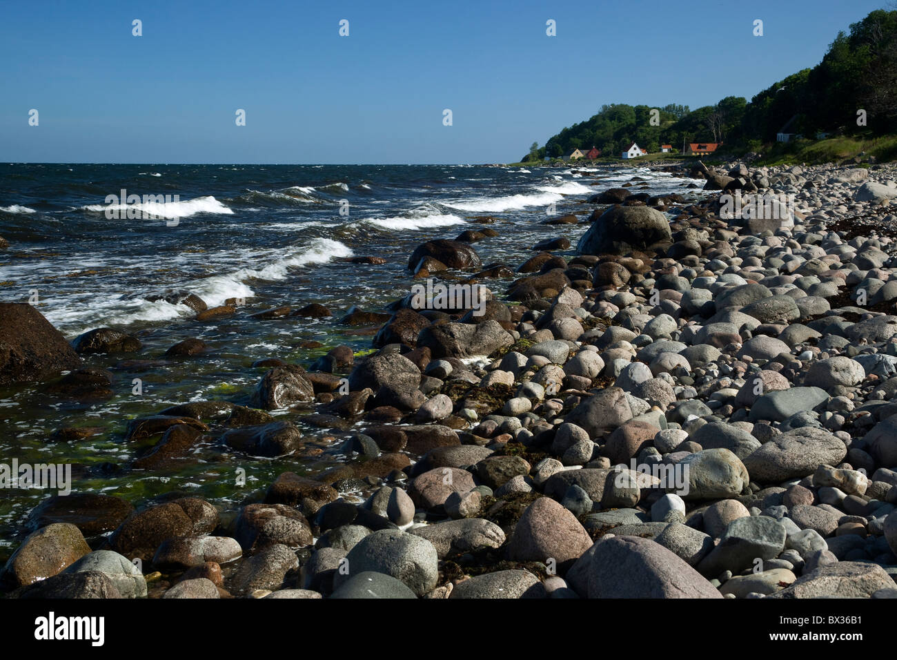 Steinige Ufer. Bornholm. Dänemark. Im Hintergrund das kleine Fischerdörfchen Helligpeder (Holypeter). Stockfoto