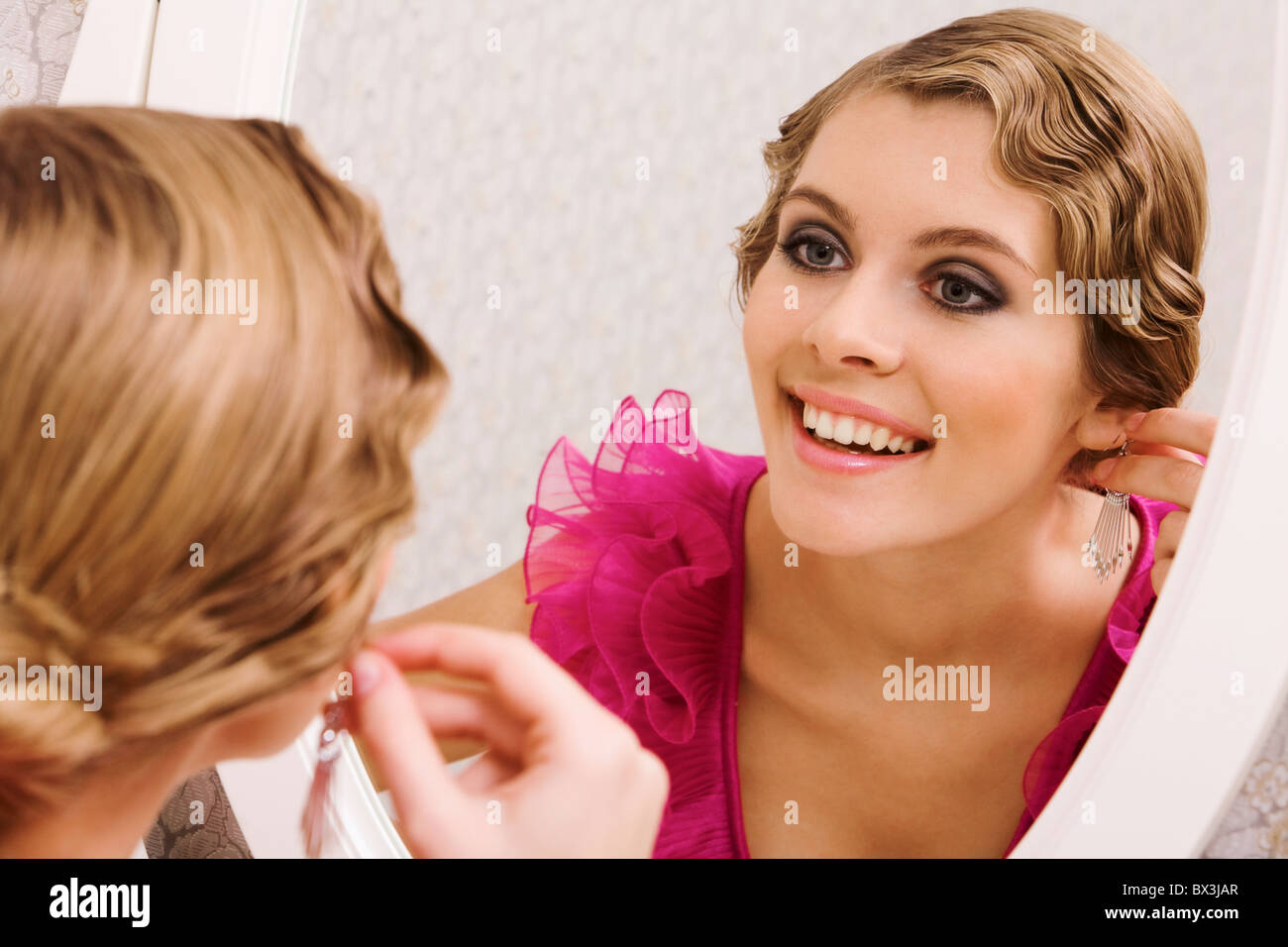Bild der hübschen weiblichen Blick in Spiegel und setzen auf Ohrringe Stockfoto