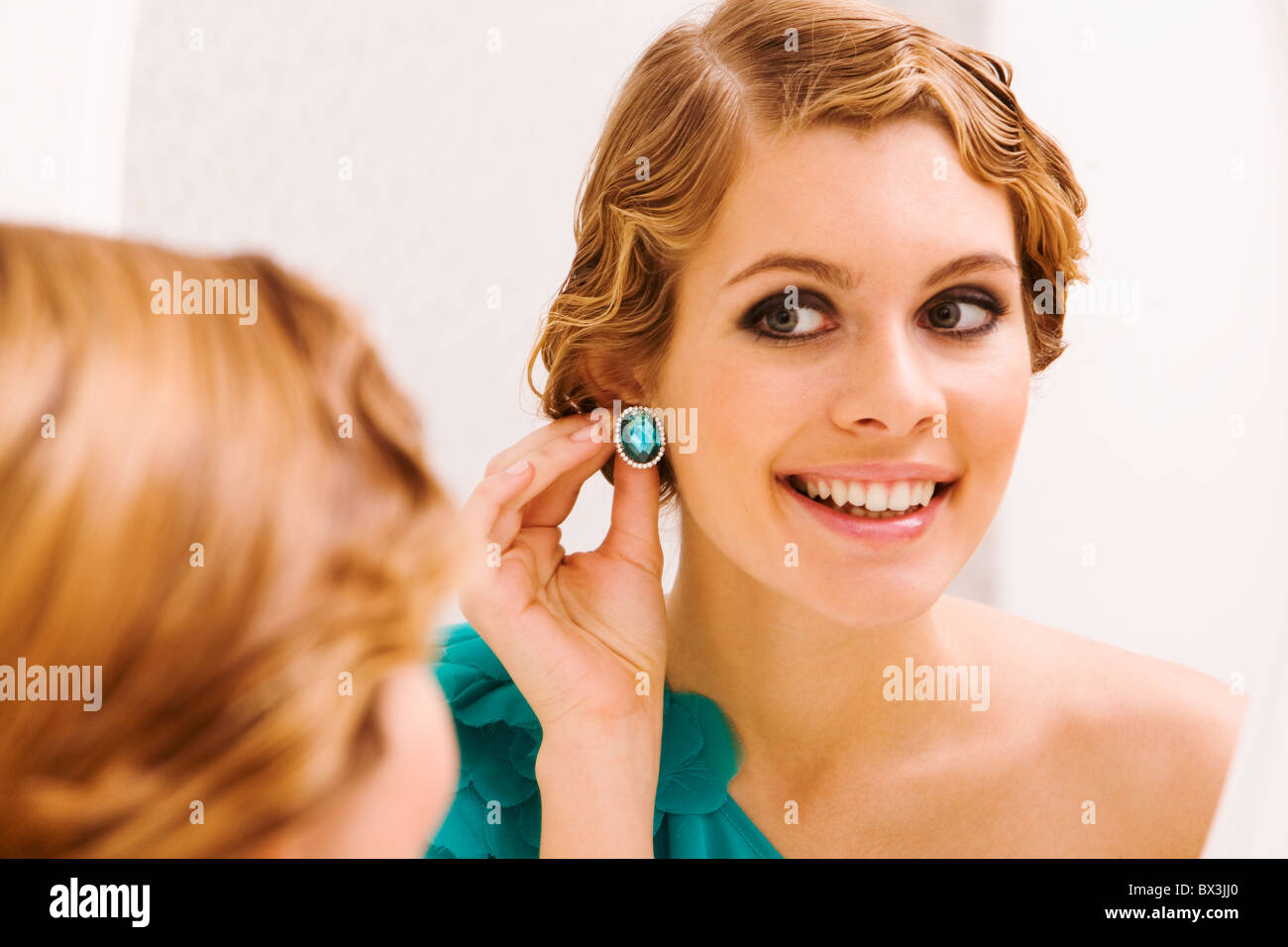 Bild der hübschen weiblichen Blick in Spiegel und setzen auf Ohrringe Stockfoto