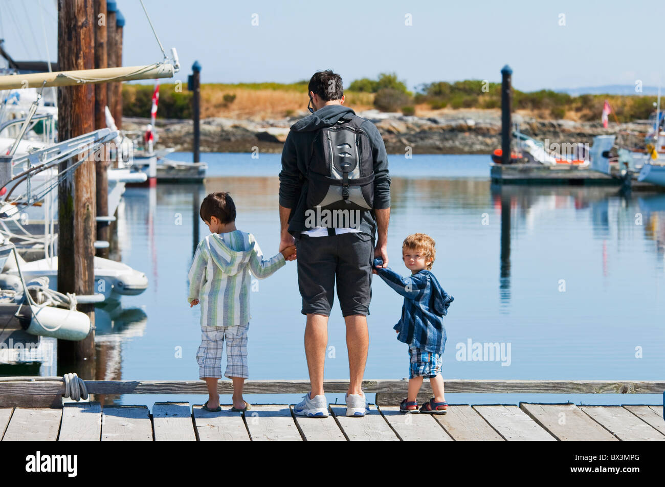 Ein Vater mit zwei Söhnen auf einem Dock Blick ins Wasser stehend; Langley, British Columbia, Kanada Stockfoto