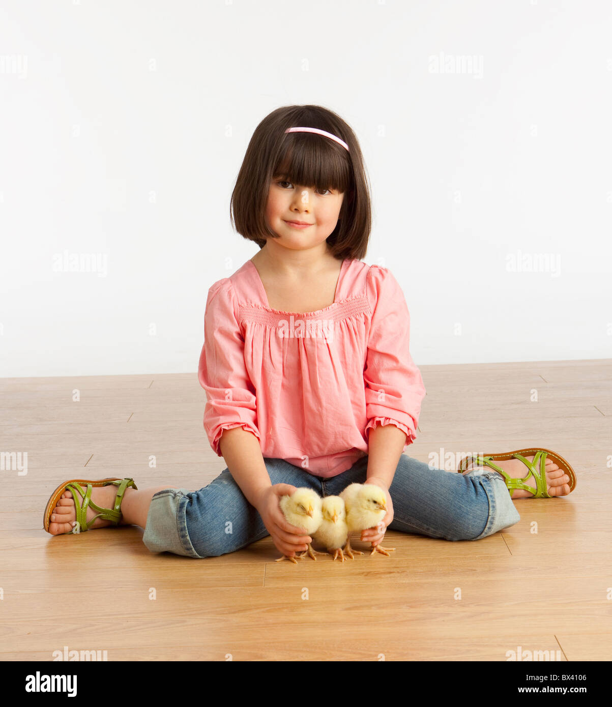 Ein Mädchen sitzt auf dem Boden mit 3 Küken Stockfoto