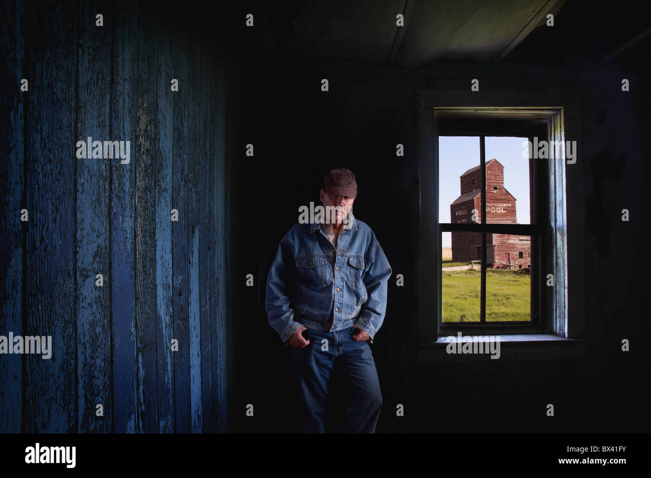 Porträt von einem Landwirt/Rancher In einem Ghost Town Store mit einem Getreidespeicher aus dem Fenster gesehen; Bents, Saskatchewan, Kanada Stockfoto