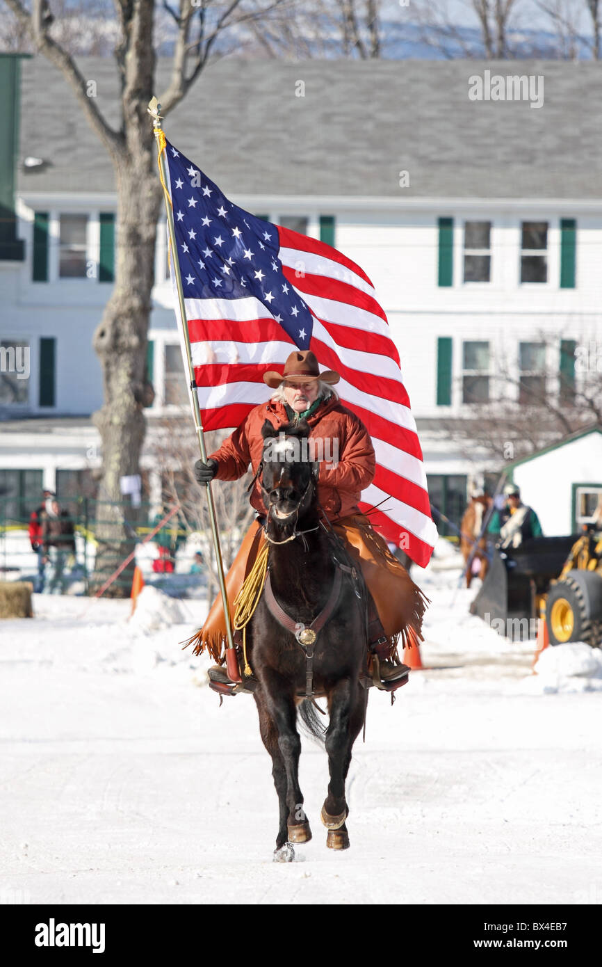 Ein Pferd und Cowboy trägt die USA-Flagge, amerikanische Flagge, während der Beginn der Veranstaltung Skijöring. Stockfoto