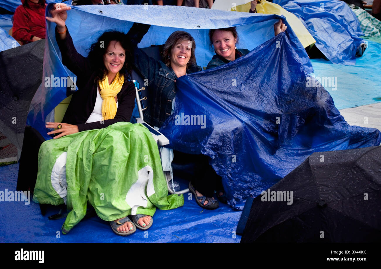 Drei Damen bei einem Outdoor-Musikkonzert (Folkfest) sich unter Tarps vor dem Regen zu schützen; Edmonton, Alberta, Kanada Stockfoto