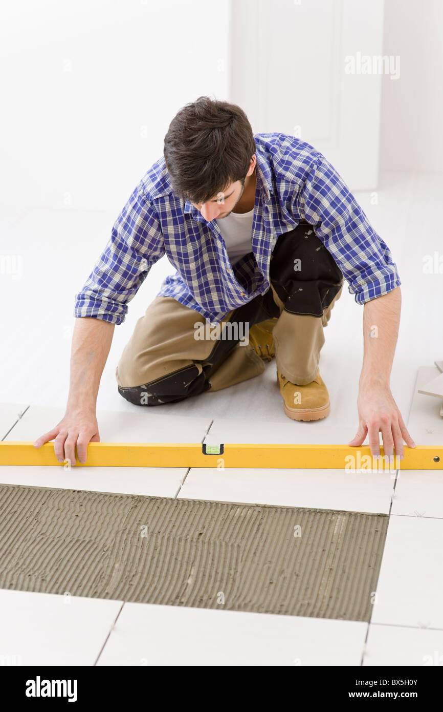 Home Fliesen Verbesserung - Handwerker mit Ebene Festlegung Fliesenboden Stockfoto