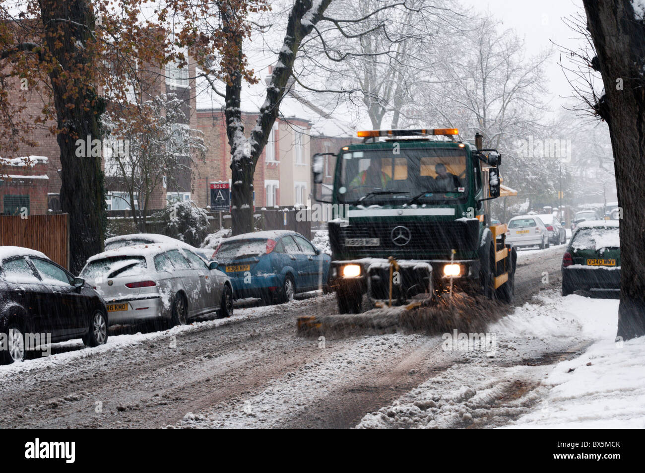 Ein abstumpfender Lastwagen, mit einem Schneepflug, Splitt oder Salz auf einer Vorstadt Straße in Südlondon während eines Schneesturms zu verbreiten Stockfoto