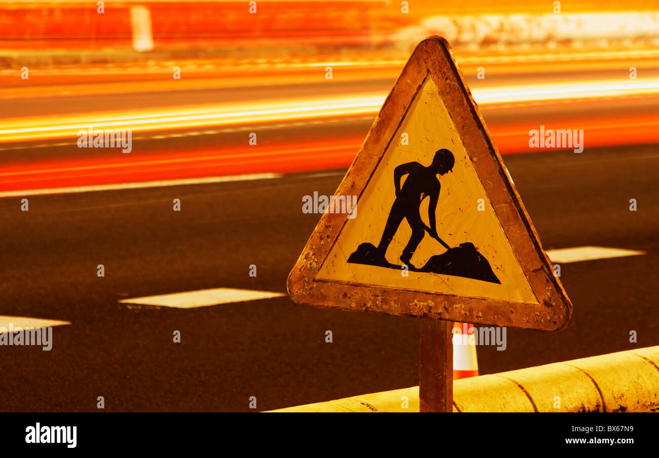Männer am arbeiten Schild am Straßenrand mit Ampel-Trails. Stockfoto