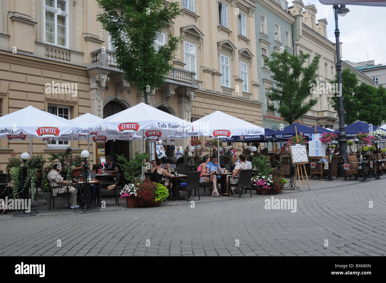 Touristen entspannen außerhalb der Bars unter Schirm im Treiben der Altstadt von Krakau in Polen, Toursit desti Stockfoto