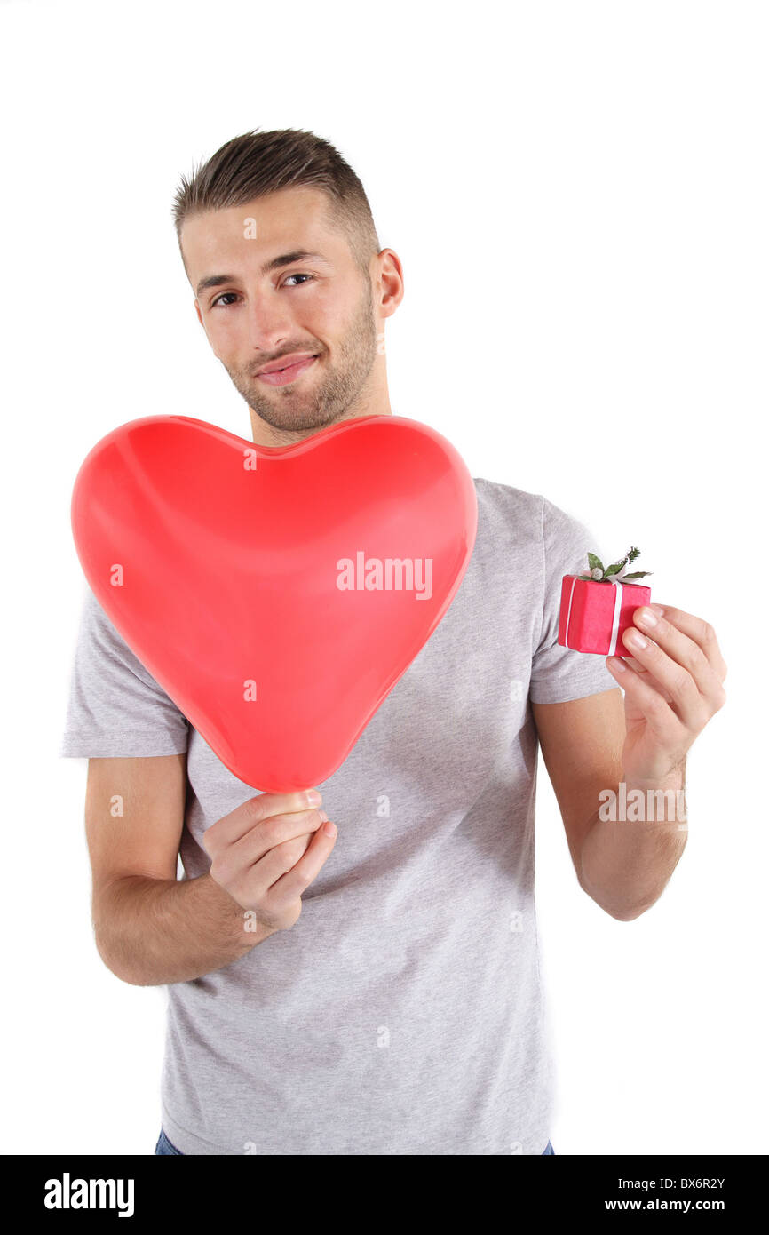 Einen schönen jungen Mann hält ein großes rotes Herz und ein kleines Geschenk am Valentinstag. Alle isoliert auf weißem Hintergrund. Stockfoto