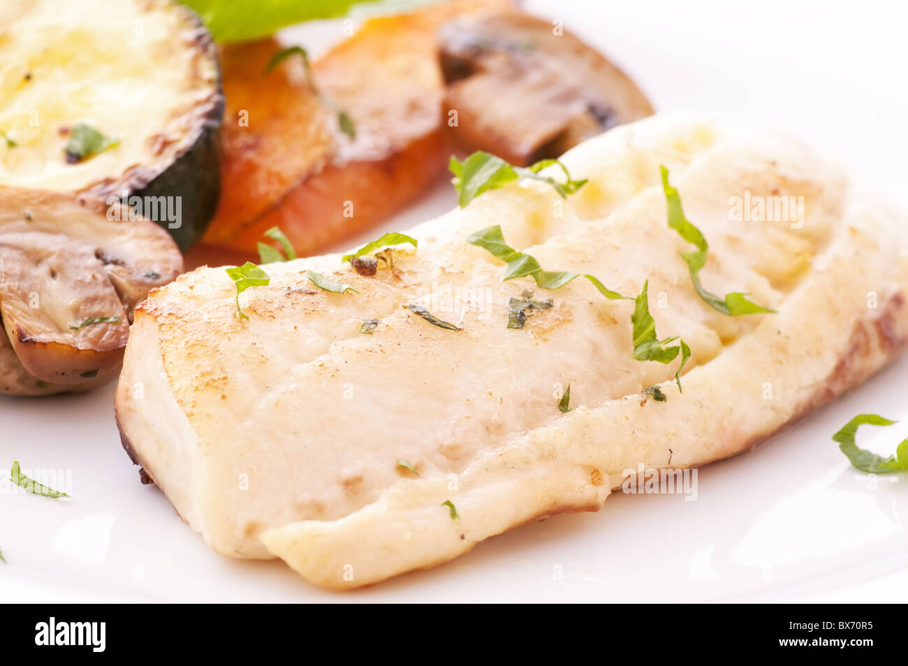 Tilapiini-Filet mit Champignons, Zucchini und Karotten als Closeup auf einem weißen Teller Stockfoto