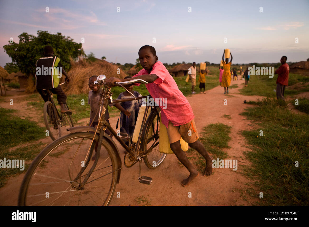 Kind Wassertragen auf einem Fahrrad in einem Dorf in Nord-Uganda, Ostafrika. Stockfoto