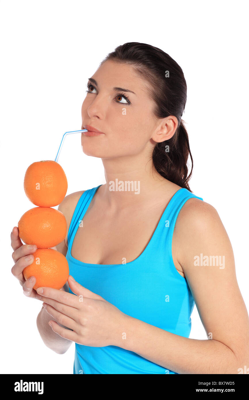 Attraktive junge Frau trinkt Orangensaft aus gestapelten Orangen. Alle auf weißem Hintergrund. Stockfoto